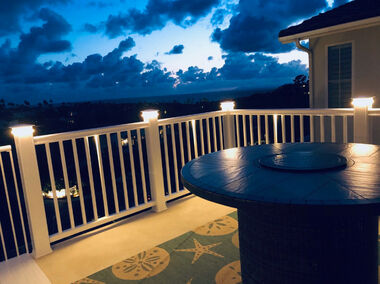 Curved white vinyl railing deck with illuminated post cap lights and scenic twilight view at dusk.