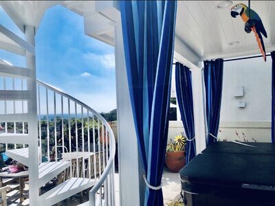 White spiral staircase connecting upper deck with covered patio, blue curtains, and ocean views.