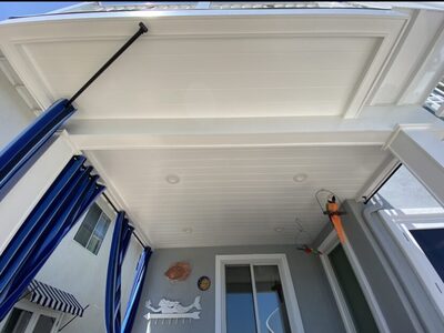 White tongue-and-groove patio ceiling with recessed lighting, blue curtains, and coastal beach-themed decor.