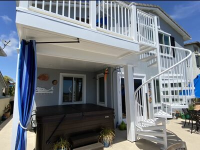 Two-story white deck with spiral staircase, hot tub below, covered patio, and blue curtain accents.